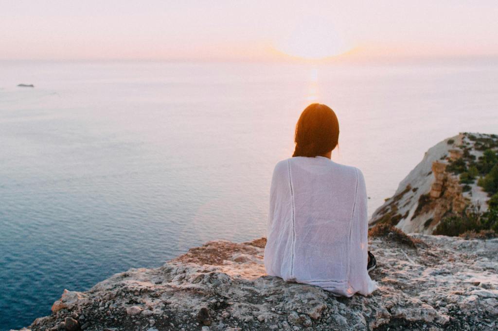 a person sitting near the shore looking off into the ocean enjoying nature