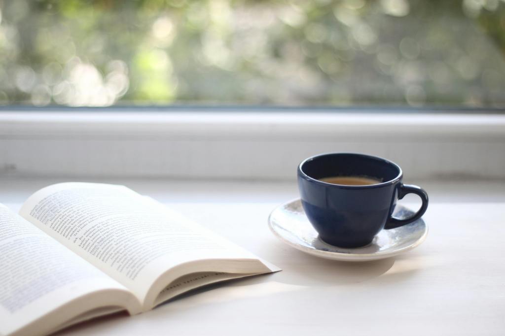 An open book and tea cup next to a window