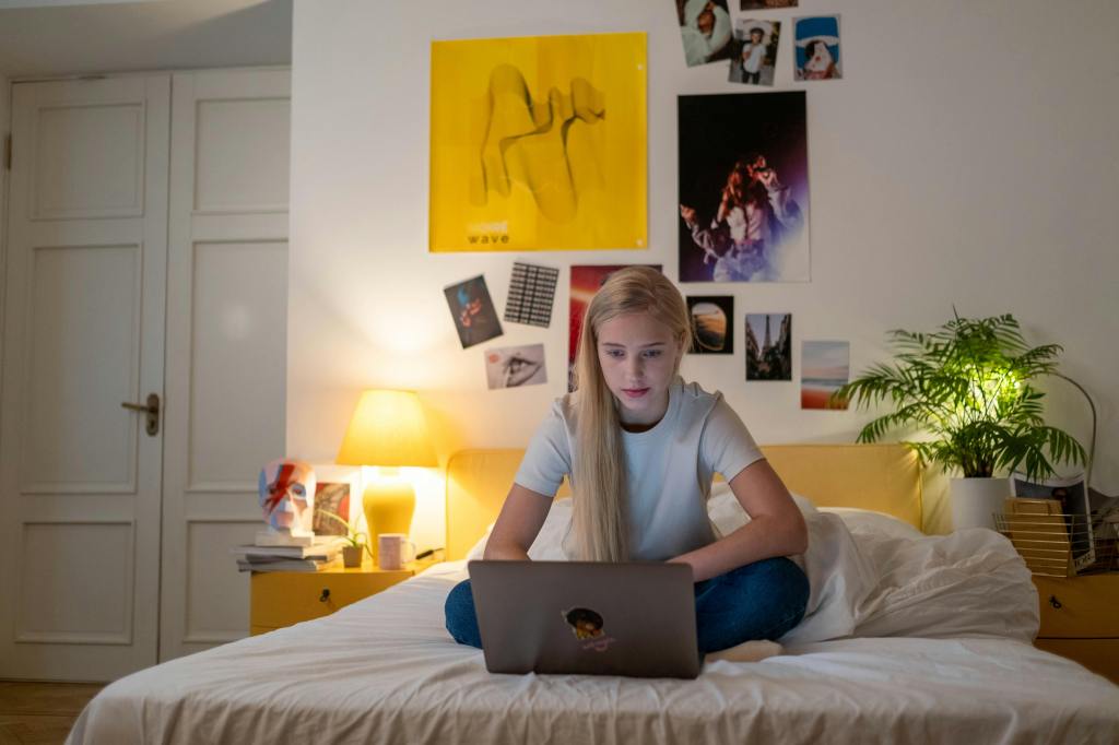 a young teenage girl sitting on her bed looking at her laptop intently