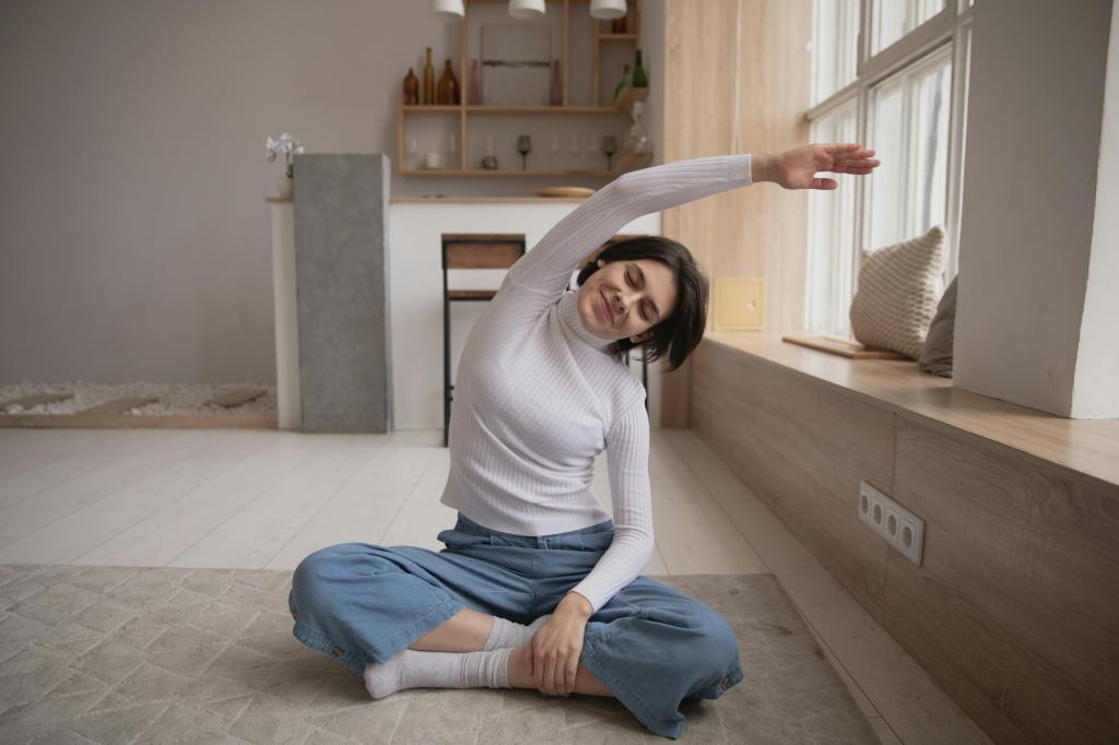 A young woman sitting and stretching in her bright-lit room.