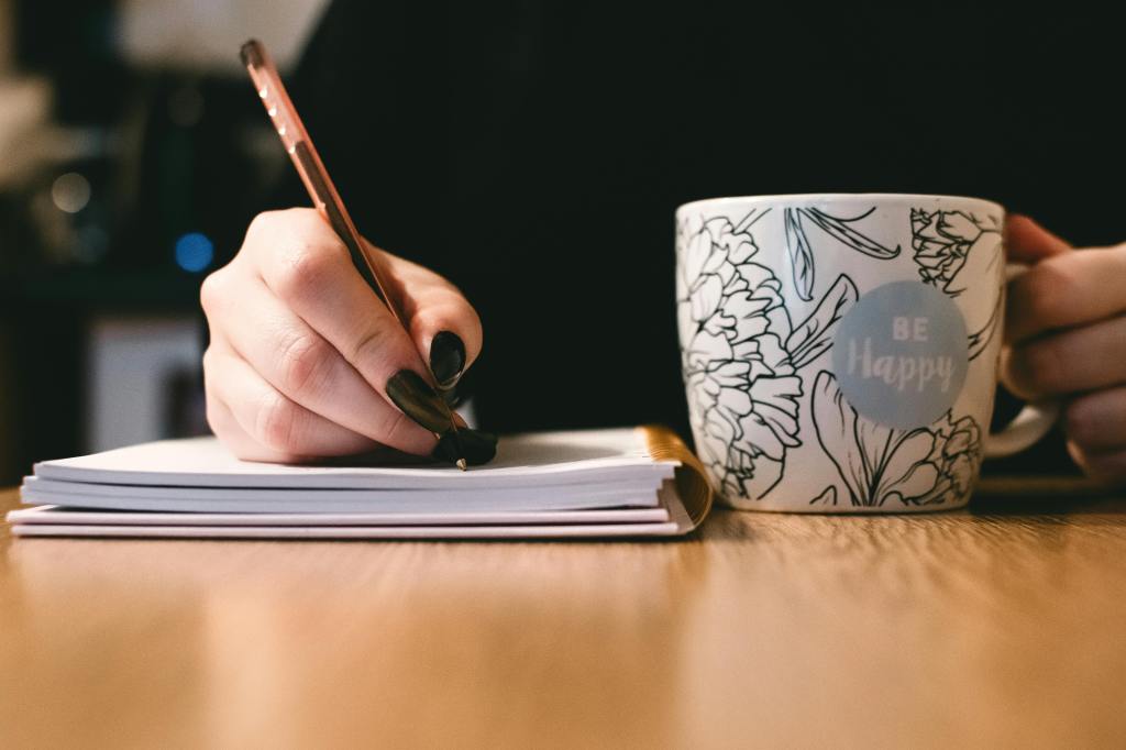A person journaling or writing with a "Be Happy" coffee mug.