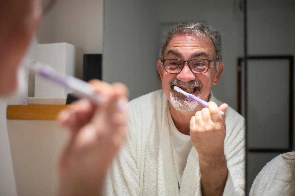 An older man brushing his teeth with a big, bright smile.
