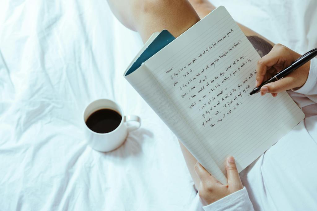 A person sitting in bed with a journal open and writings down and coffee nearby.