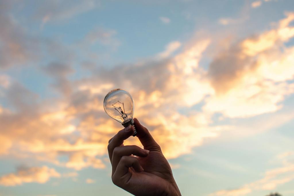 A person holding a lightbulb up to the sky outside.