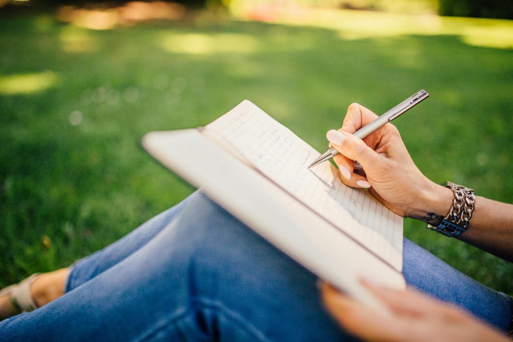 A young woman writing in her journal while outside in nature.