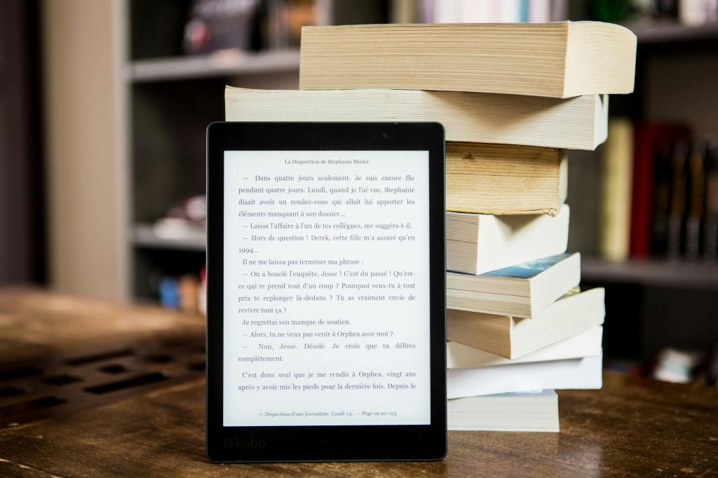 A e-book reader open to a page resting against a stack of books.