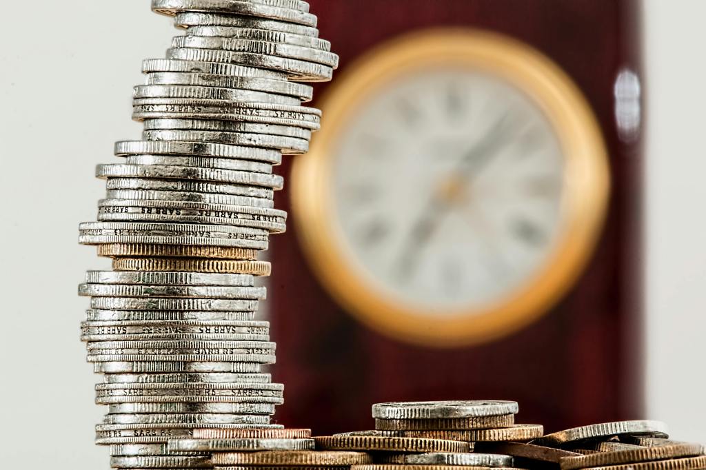 A stack of coins in front of a clock