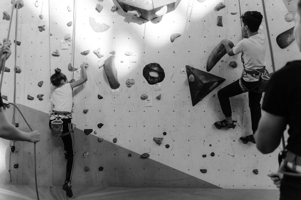 a girl and a boy climbing a wall at a wall climbing gym